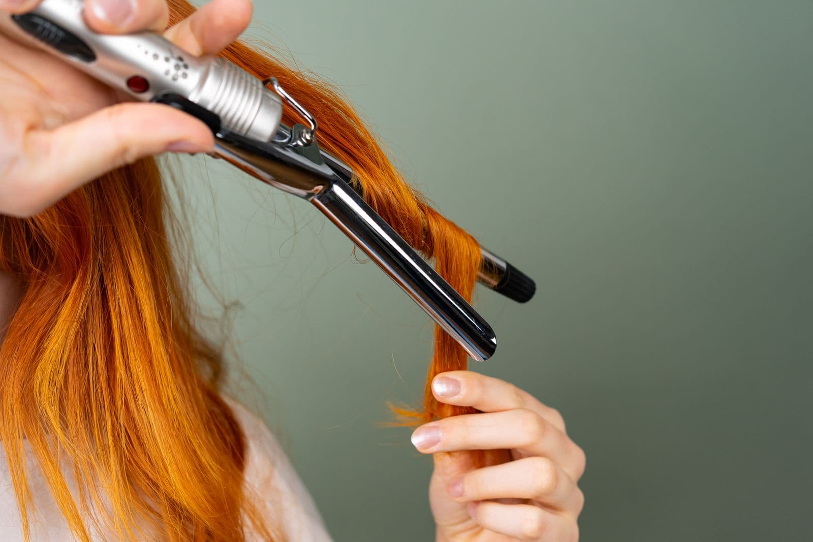 A section of red hair being curled around a styling iron