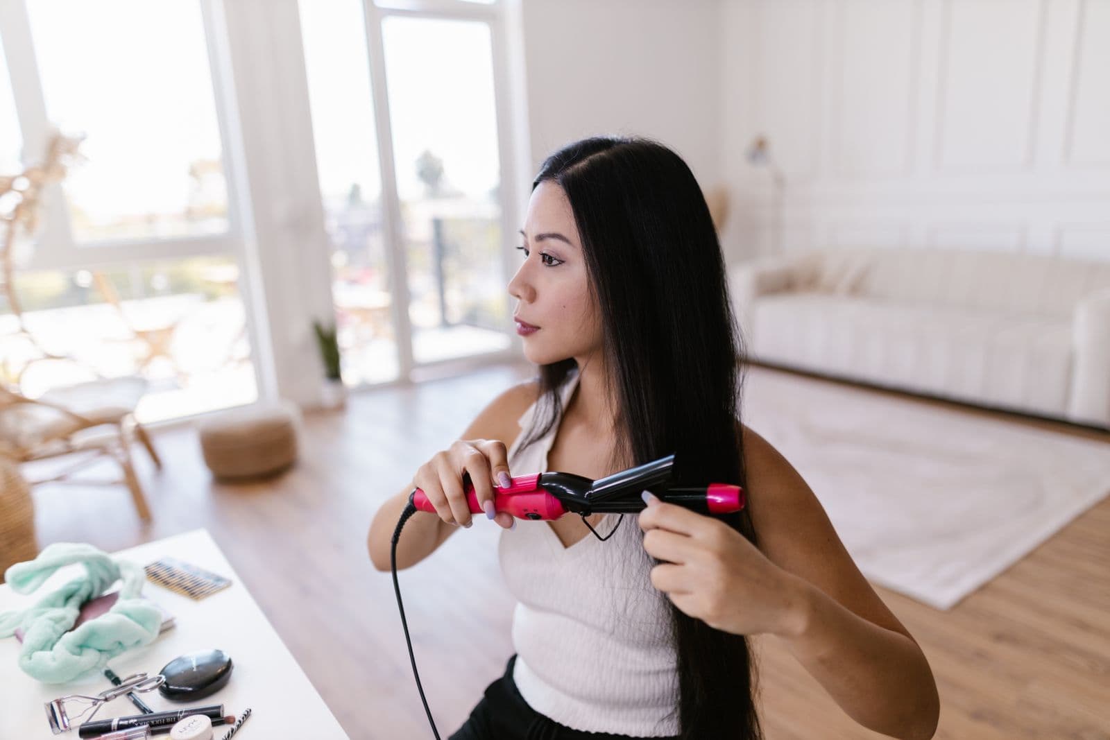 A woman straightening her long hair with a flat iron at home