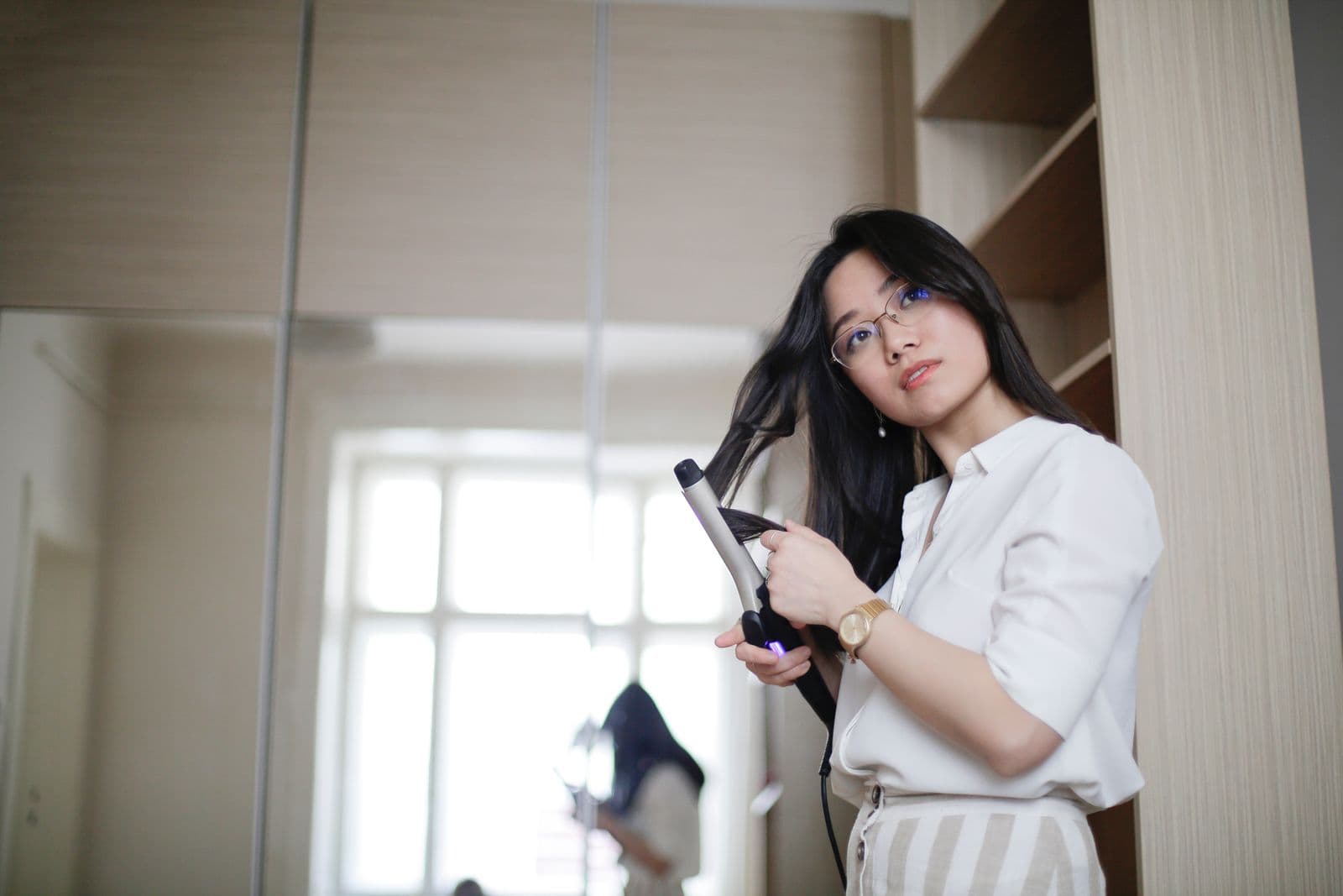 A woman curling her hair with a styling iron at home